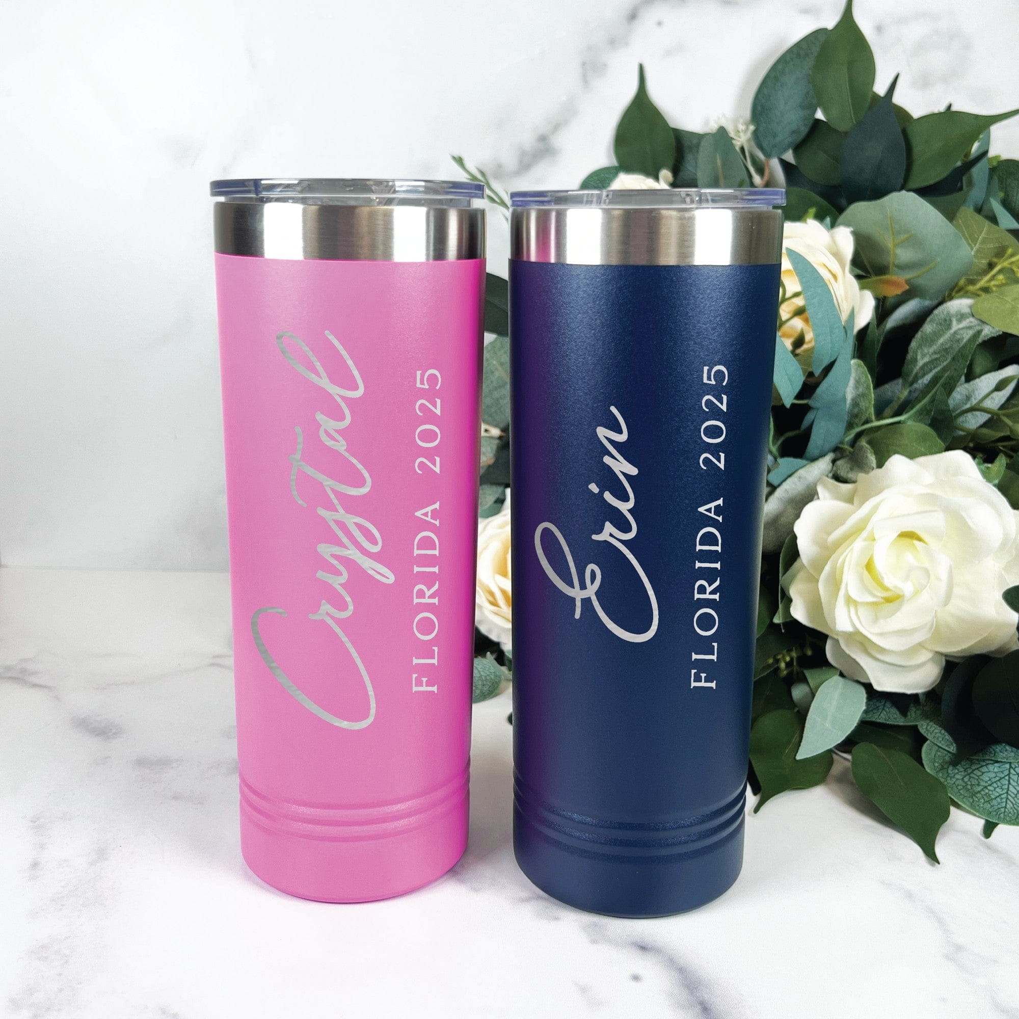 Two personalized insulated stainless steel tumblers, one in a matte pink finish and the other in a matte navy blue, featuring silver accents and clear plastic lids, suitable for a wedding party or special event.