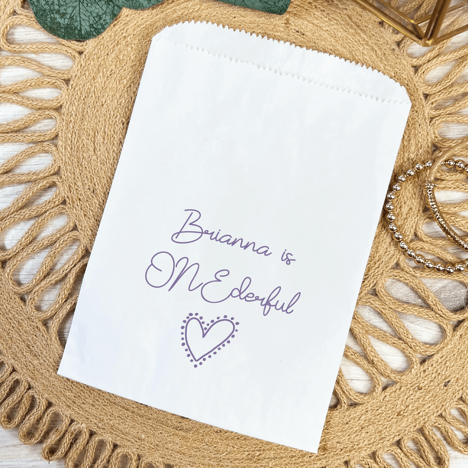 White treat bag with "Brianna is ONEderful" text and purple heart design on woven placemat