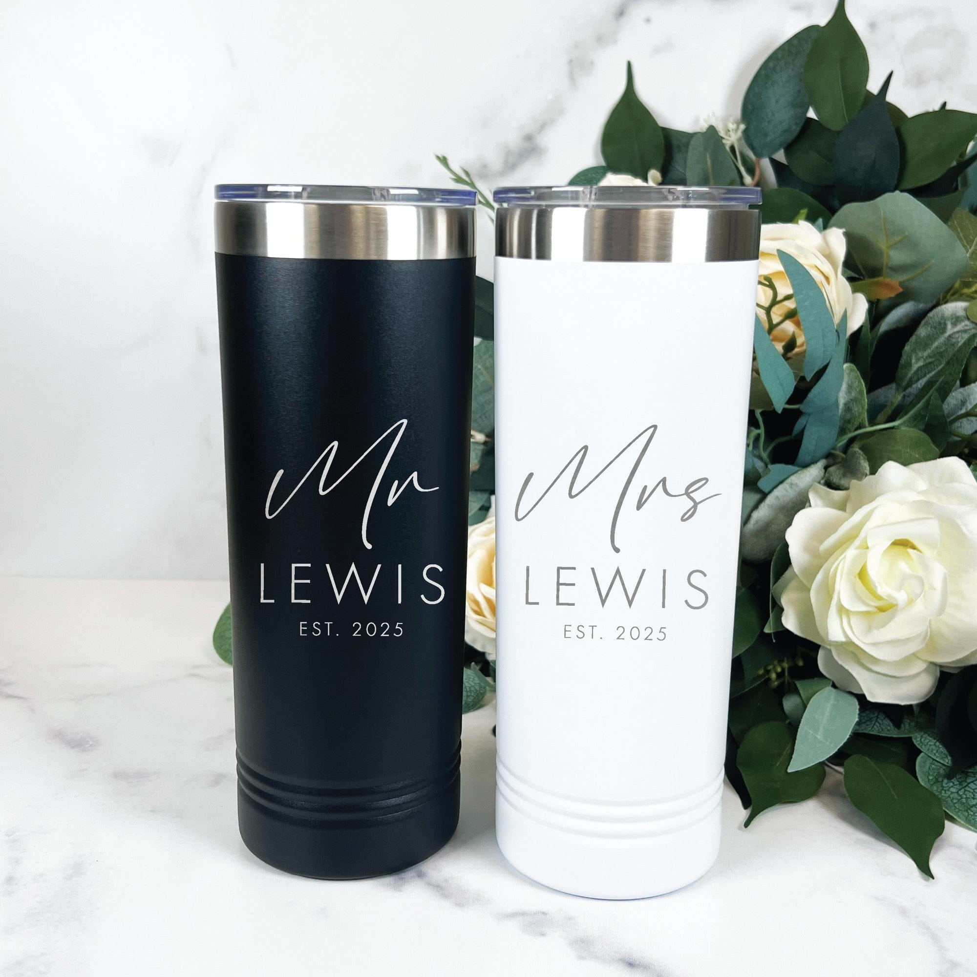 A matching set of a black and a white insulated stainless steel tumbler, each with a silver rim and clear lid, designed as personalized drinkware for a bridal or wedding event.