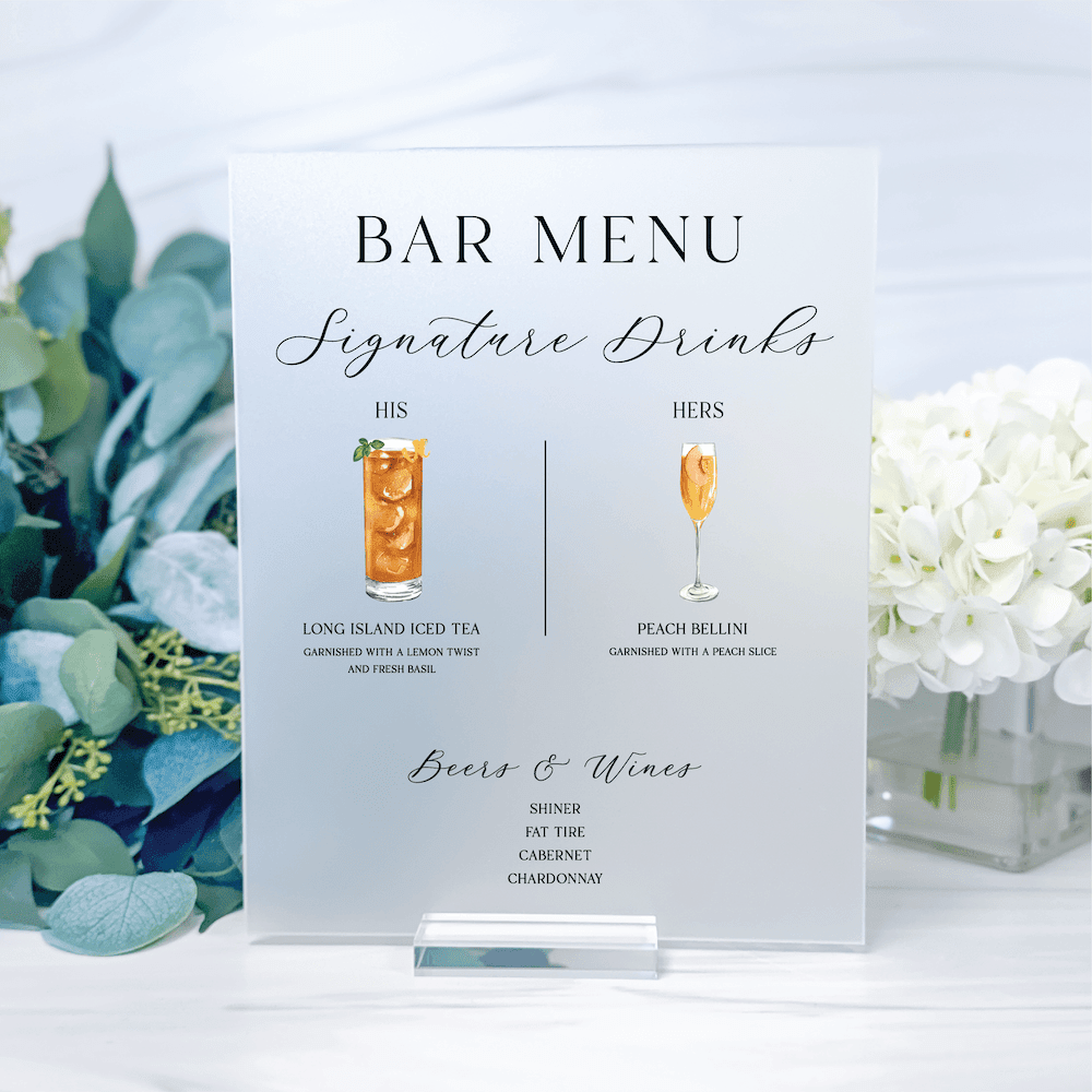 Elegant acrylic bar menu sign displaying signature cocktails and wine selections with illustrated drink graphics and greenery arrangement.