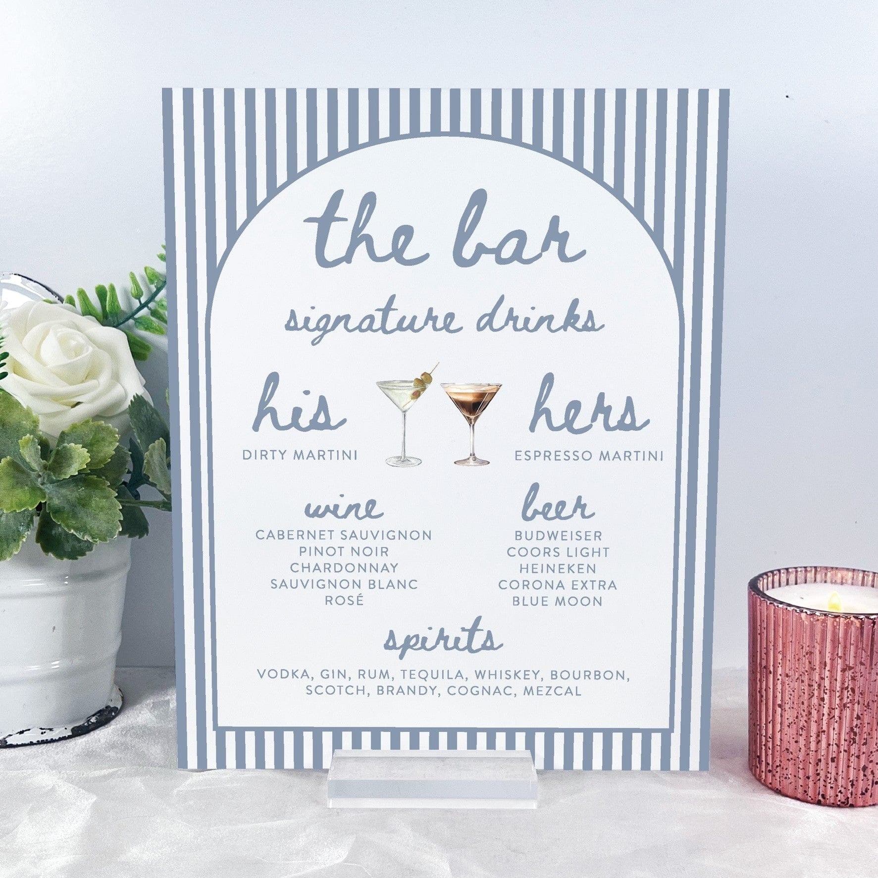 A white and light blue striped wedding bar menu sign with an arched design, made from a rigid material and displayed on a clear acrylic stand, listing signature drinks, wine, beer, and spirits for a wedding or special event.