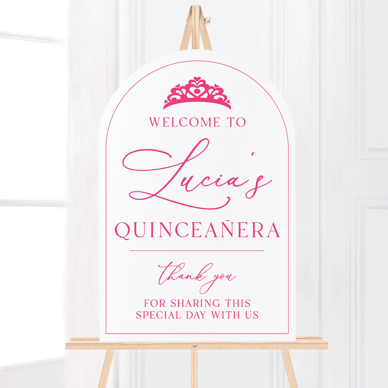 White arched welcome sign with pink text and tiara design reading "Welcome to Lucia's Quinceanera thank you for sharing this special day with us" on wooden easel.