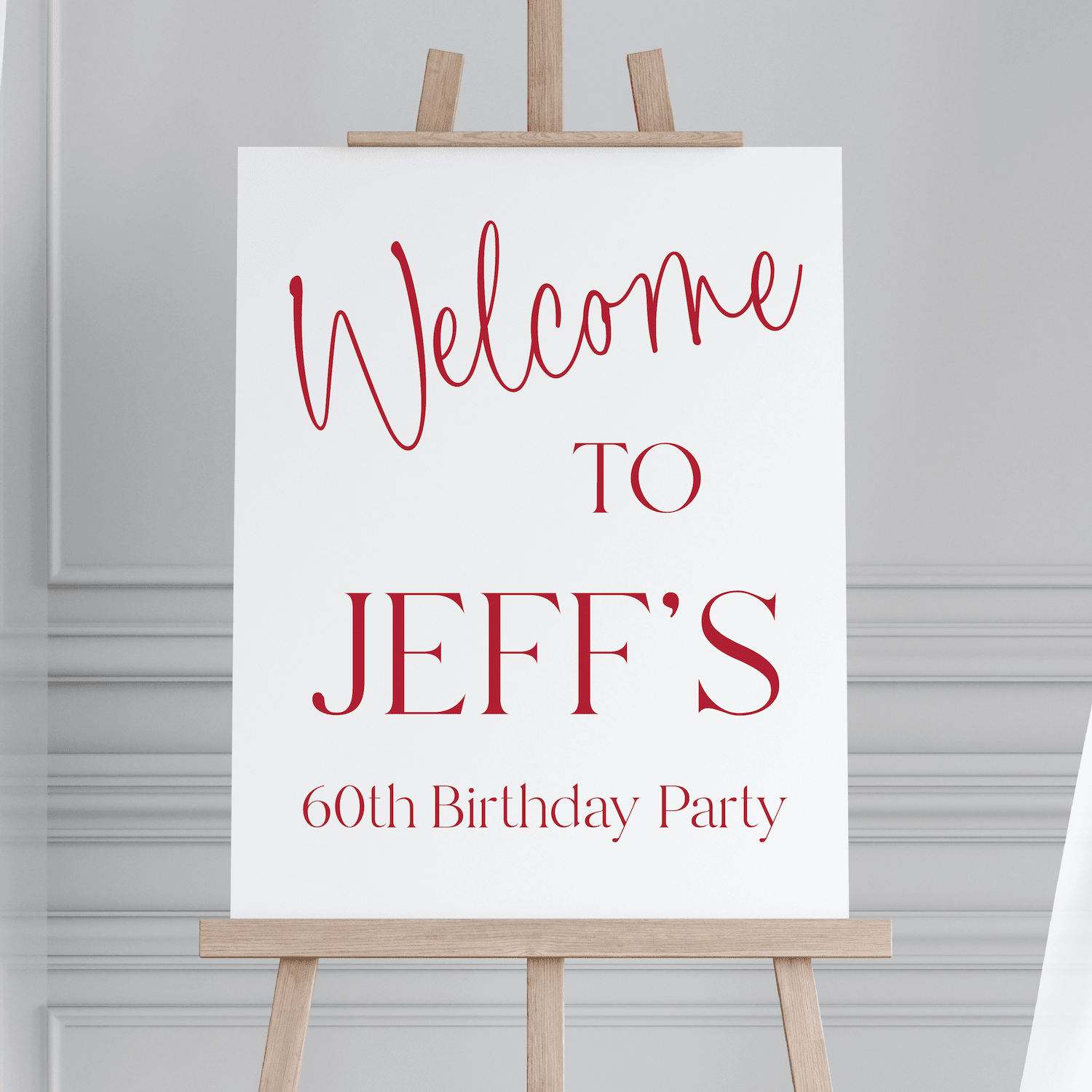 White welcome sign with red script text reading "Welcome to Jeff's 60th Birthday Party" displayed on wooden easel