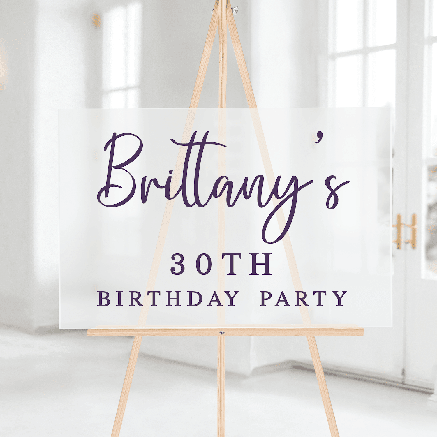 White welcome sign with "Brittany's 30TH BIRTHDAY PARTY" in navy script and block lettering, displayed on natural wood easel
