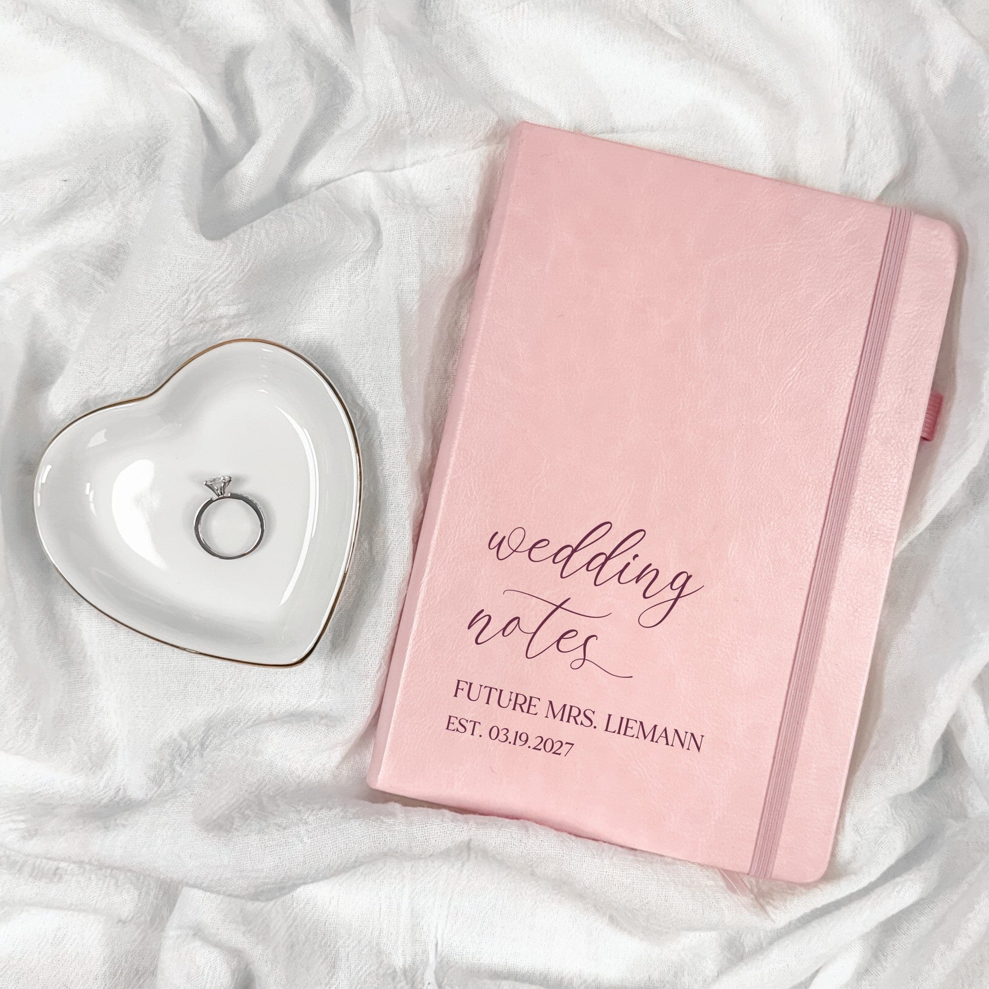 A light pink textured notebook with an elastic band closure and a matching fabric bookmark, perfect for organizing wedding planning details.