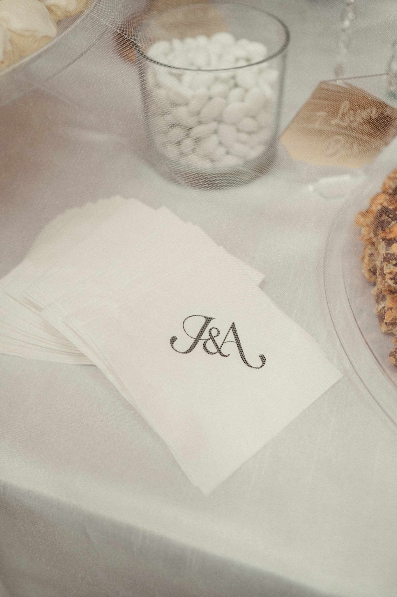 Elegant cream-colored fabric napkins with personalized dark embroidery, thoughtfully displayed as part of a sophisticated event table setting.