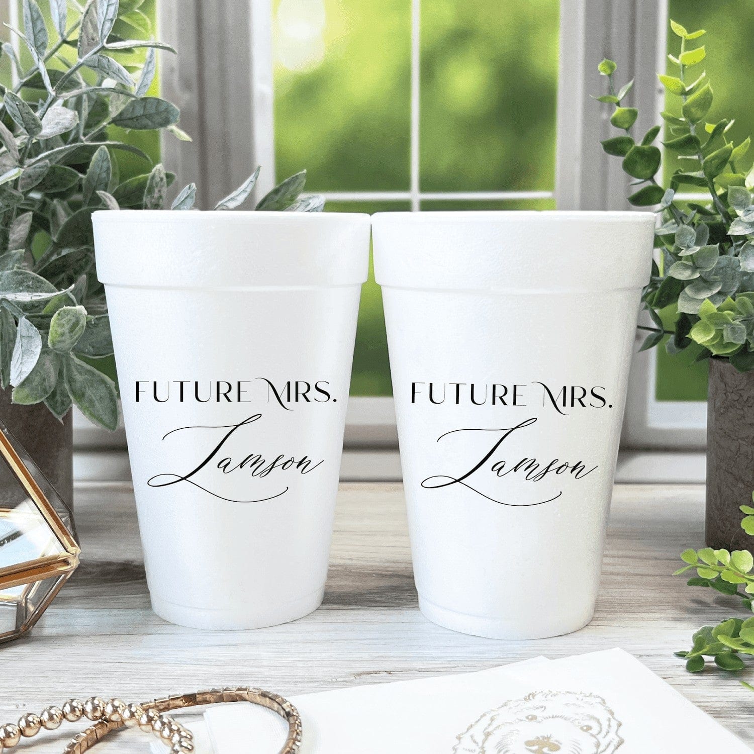 Two personalized white insulated party cups featuring Future Mrs. text and a custom name, displayed in a charming setting with plants.
