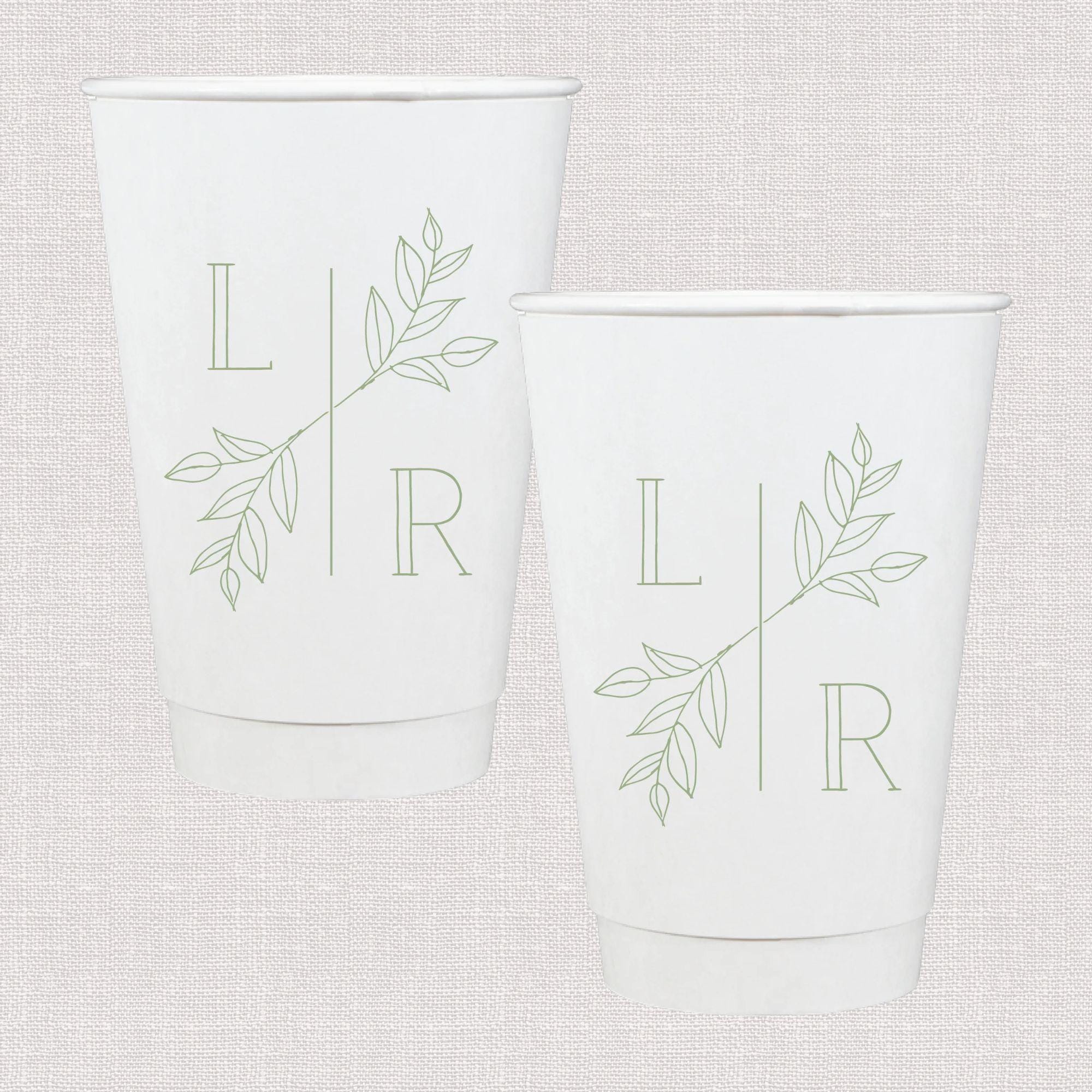 Two white paper cups with personalized initials L and R separated by a vertical line, decorated with delicate green leaf designs.