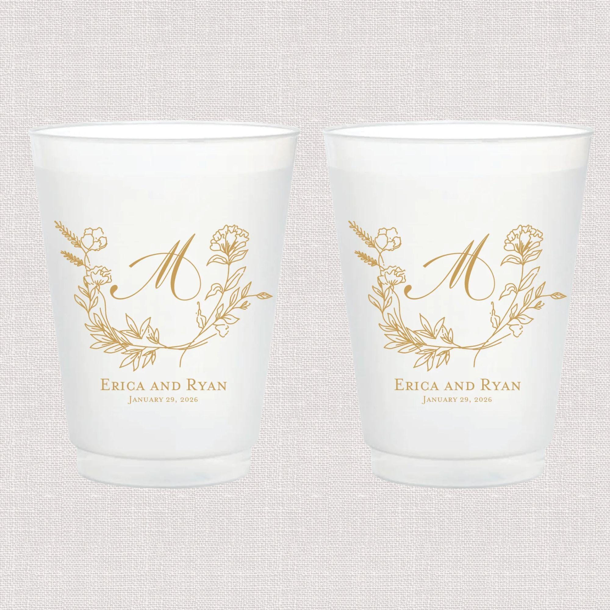 Pair of frosted plastic cups with gold botanical design and "M" monogram, personalized with "Erica and Ryan" wedding names below.