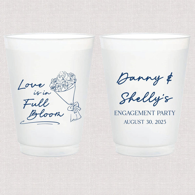 Pair of frosted white cups with blue text, one featuring "Love Is In Full Bloom" with floral design, the other personalized "Danny & Shelly's Engagement Party August 30, 2025"