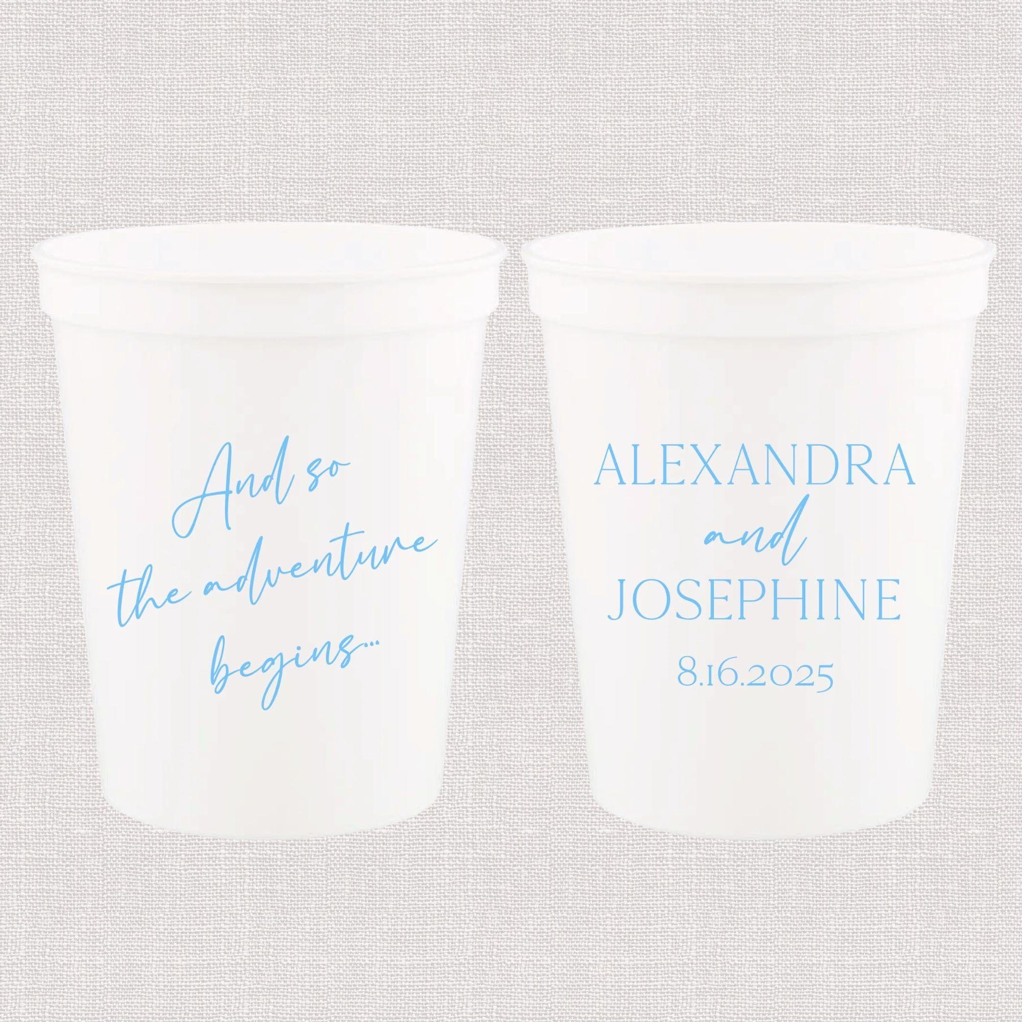 Two white stadium cups with light blue text, one reading "And so the adventure begins" and the other personalized with "ALEXANDRA and JOSEPHINE 8.16.2025"