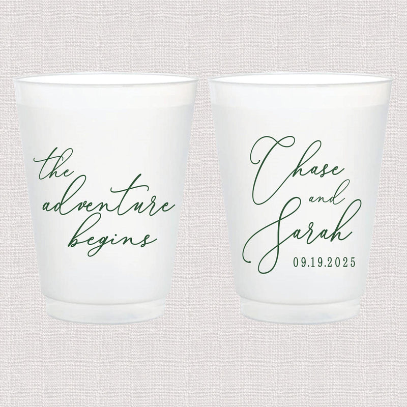 Pair of white frosted cups with cursive text, one reading "the adventure begins" and the other personalized with names and wedding date