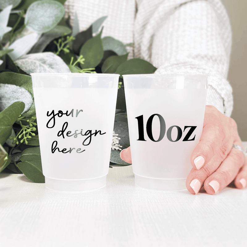 Two frosted 10oz cups held in hands with green eucalyptus, one showing "your design here" text and the other displaying "10oz" size marking.