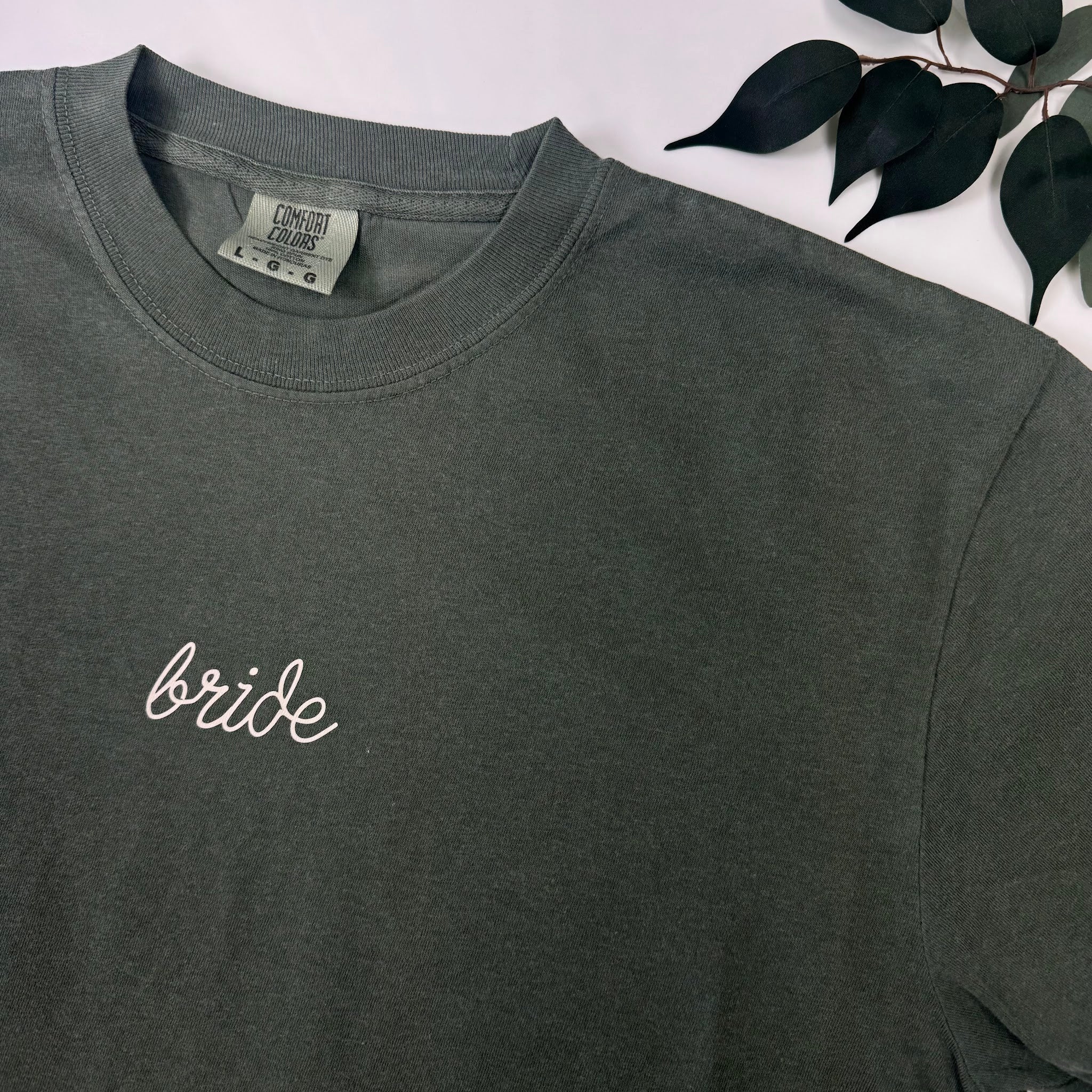 Hunter green embroidered Bride t-shirt, angled view showing garment dye texture and embroidery detail