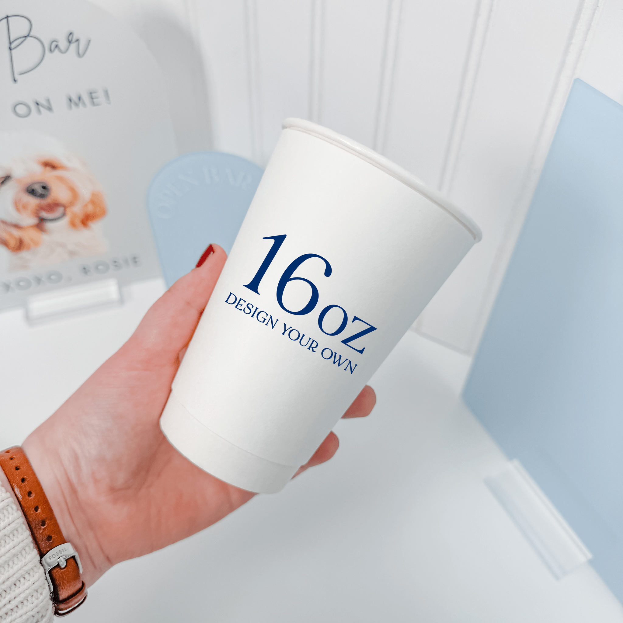 Hand holding a 16 oz white paper cup with a design your own navy print, shown for size