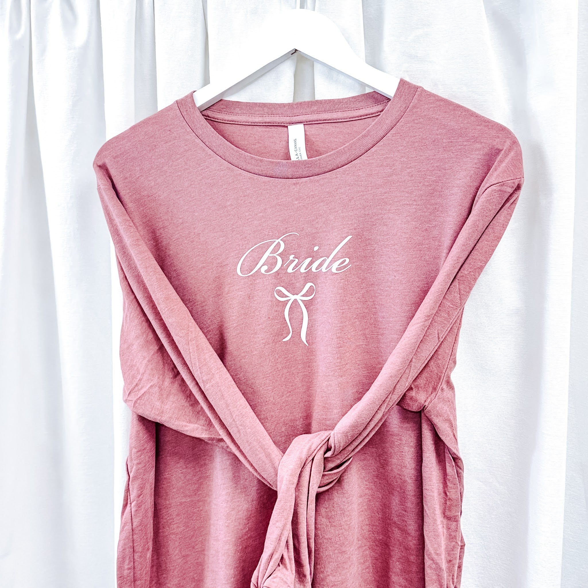 Mauve Bella Canvas long sleeve bride tee with white Bride script and bow design on hanger