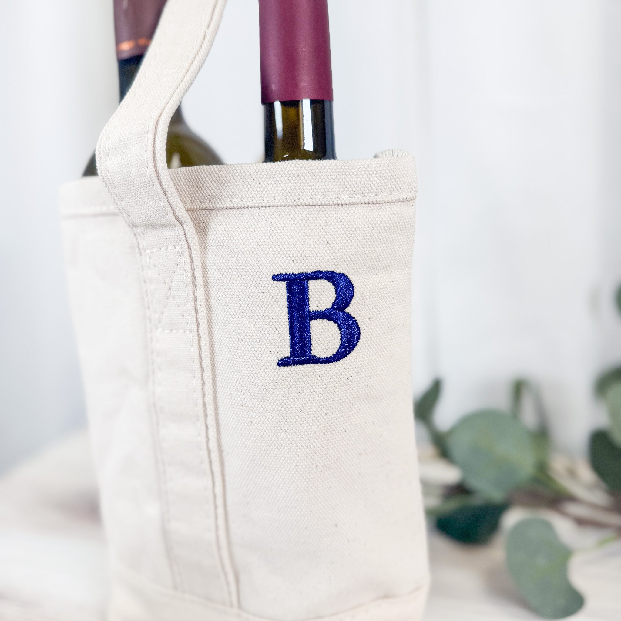 Close-up of custom embroidered B monogram in royal blue on natural canvas wine tote bag