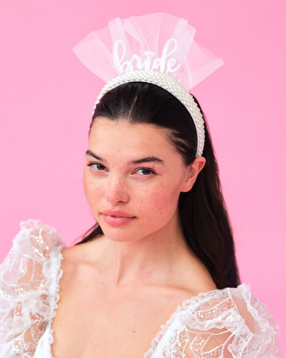 White pearl-beaded headband with "bride" text and pink tulle fan detail, worn on model against pink background.