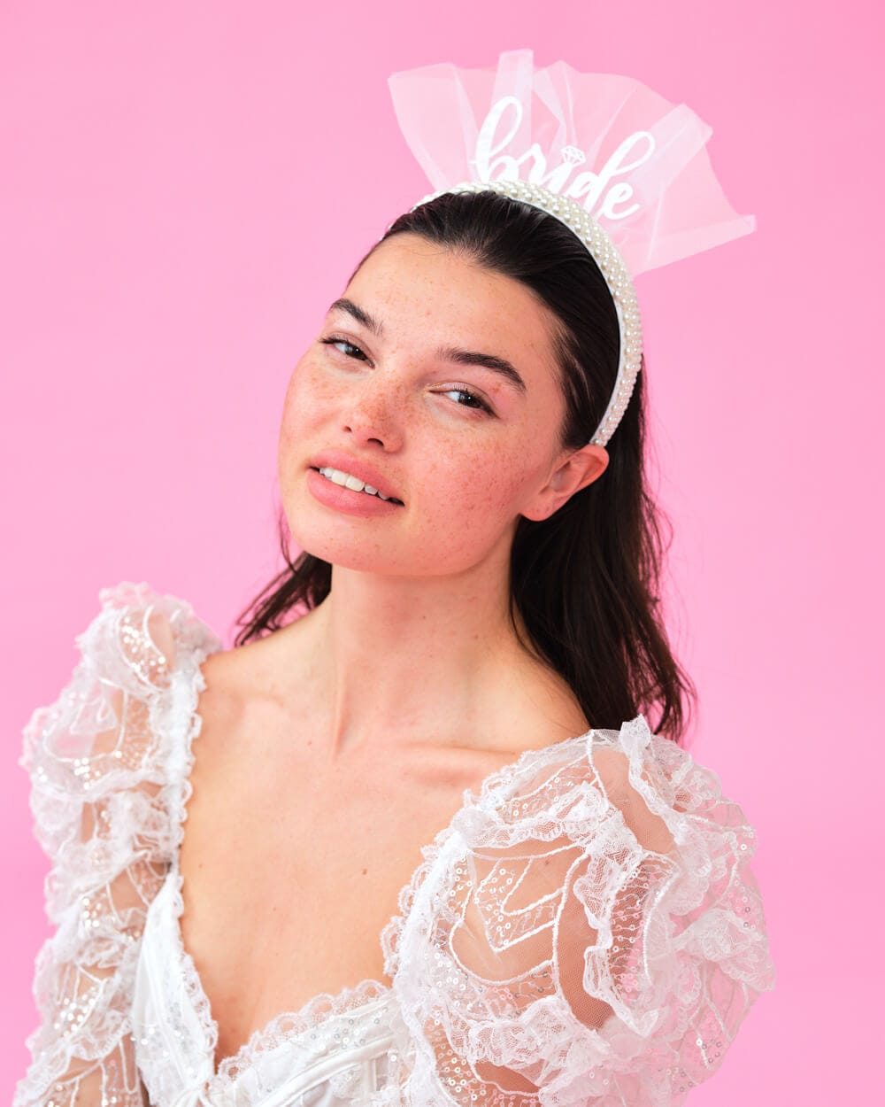 White bride headband with pearl embellishments and tulle bow, featuring script text on pink background
