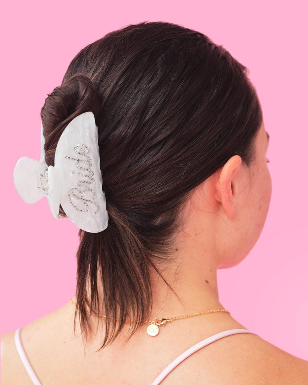 White pearlescent claw hair clip with "That Bride" text, worn in dark hair against pink background.
