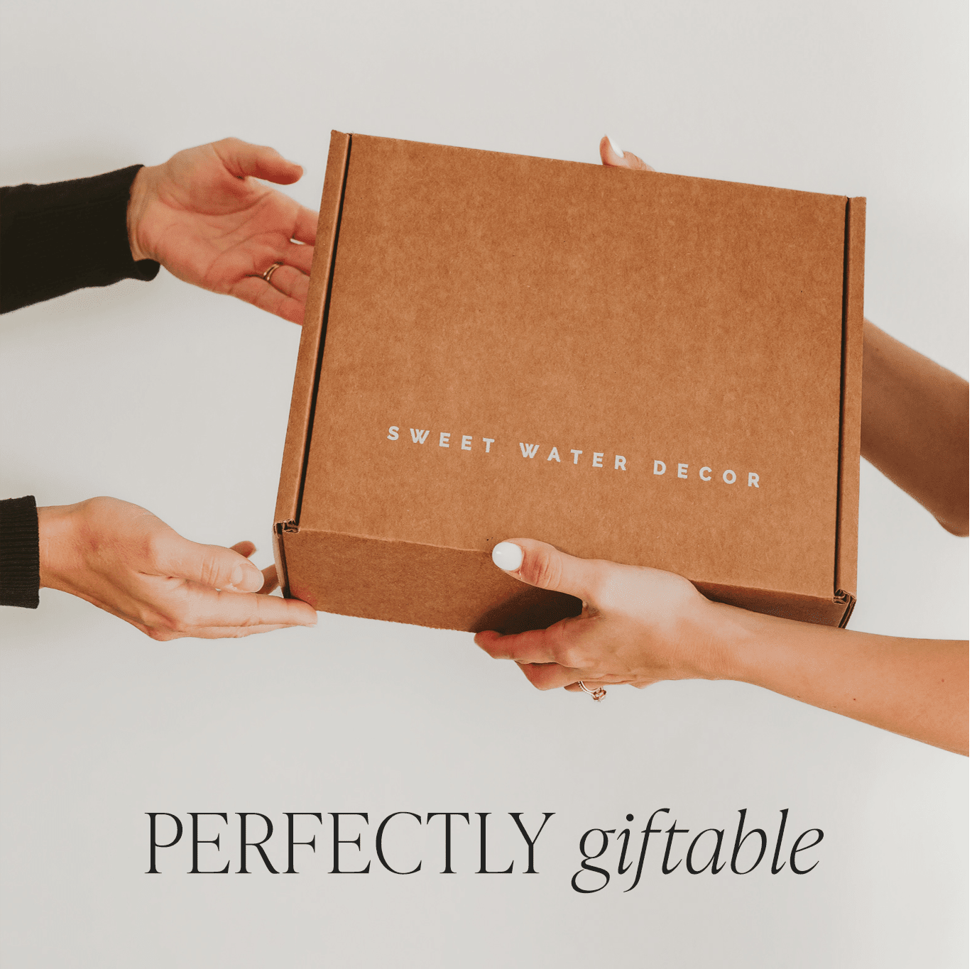 Kraft cardboard gift box with "Sweet Water Decor" text, held by two pairs of hands, with "Perfectly giftable" text below