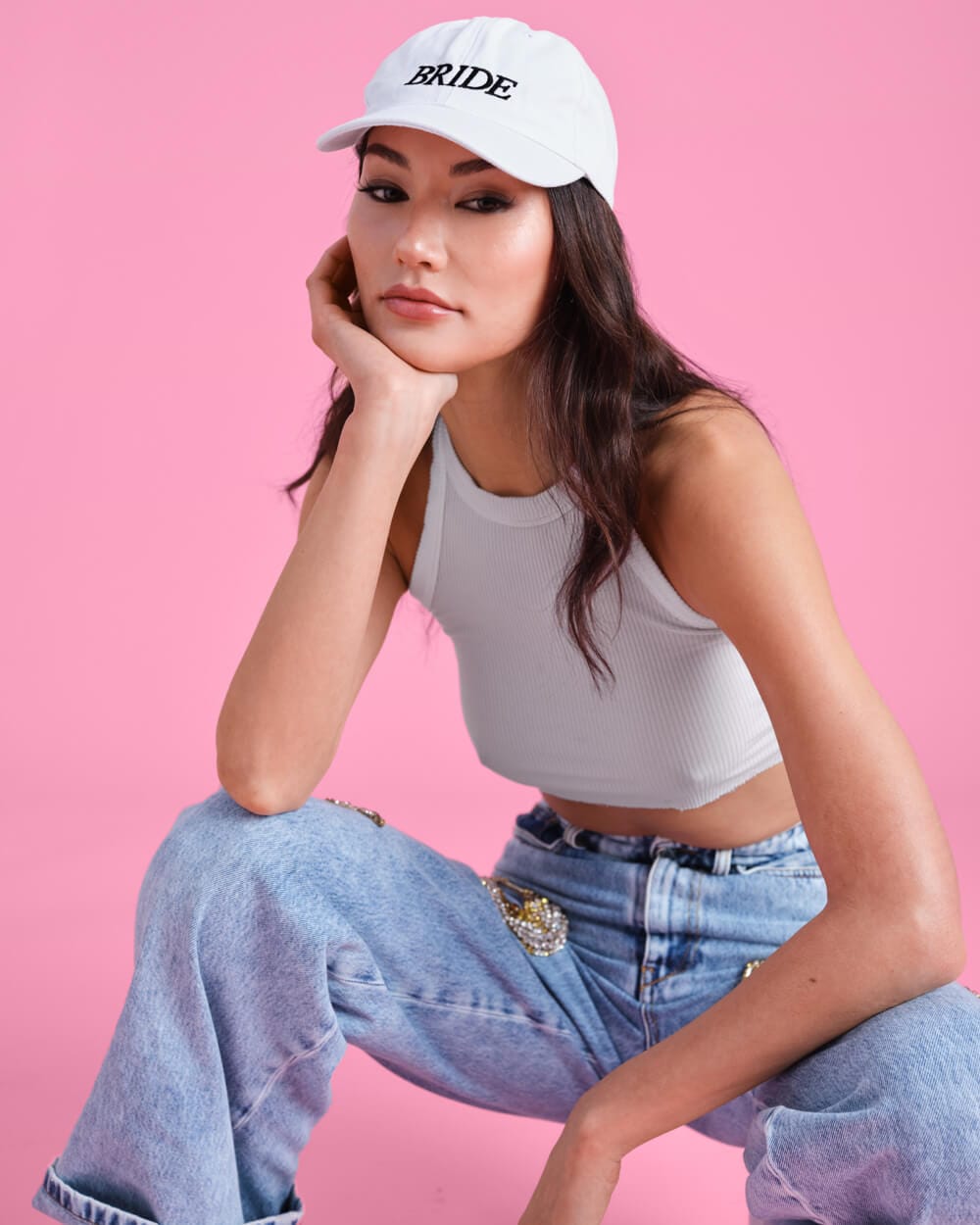 White baseball cap with "BRIDE" embroidered text, worn by woman against pink background.