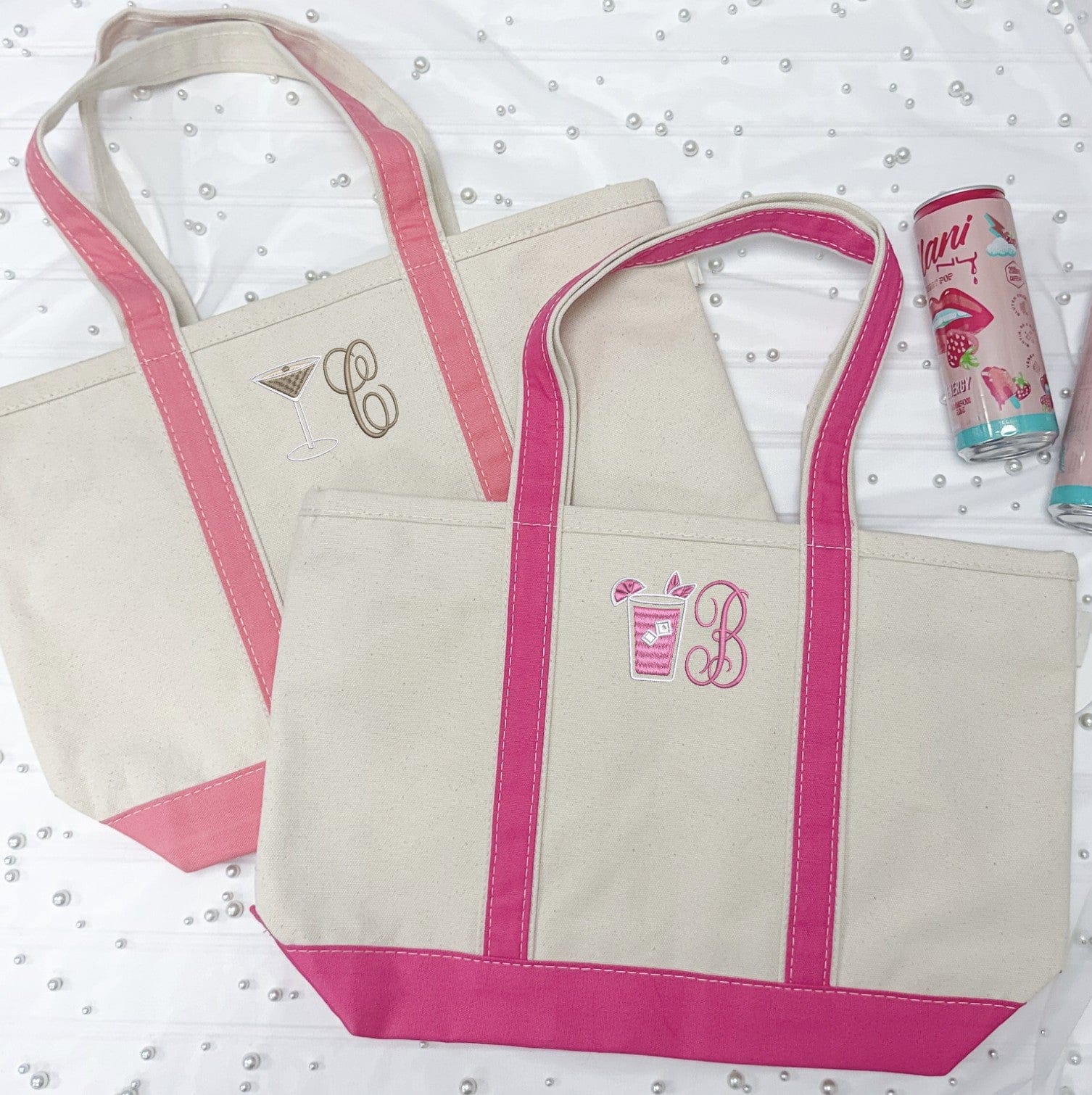 Two personalized natural canvas tote bags with hot pink handles and bases, featuring embroidered cocktail designs and single letter monograms, ideal for wedding party gifts or bachelorette celebrations.