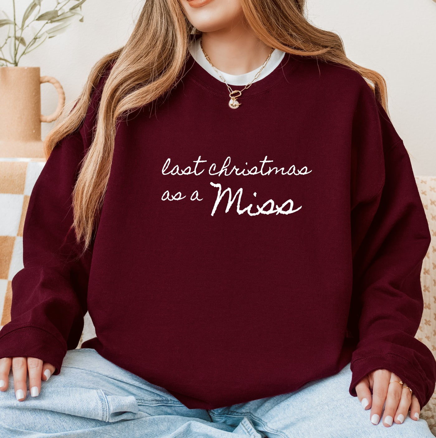 A cozy maroon crewneck sweatshirt made of soft fabric, featuring custom white script text, suitable for a bride-to-be during the Christmas season.