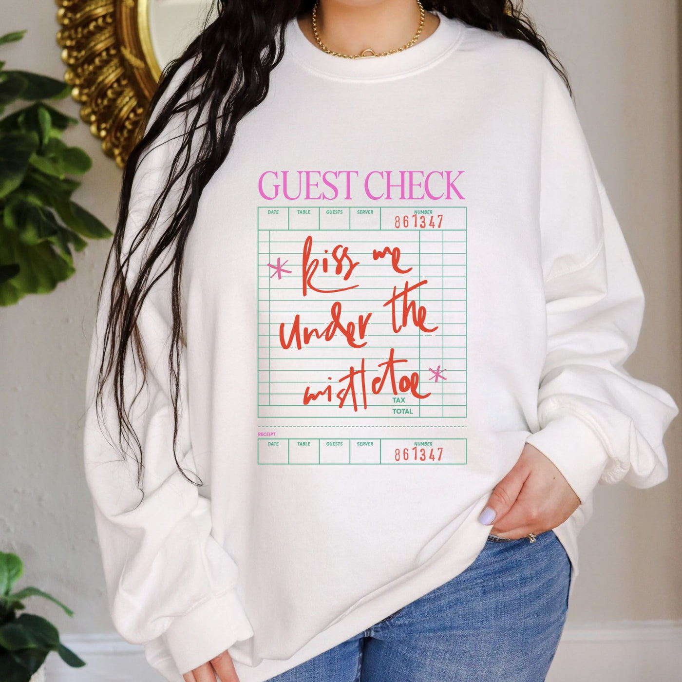 A white crewneck sweatshirt featuring a holiday-themed guest check graphic with the phrase 'Kiss me under the mistletoe' in red, perfect for festive celebrations.