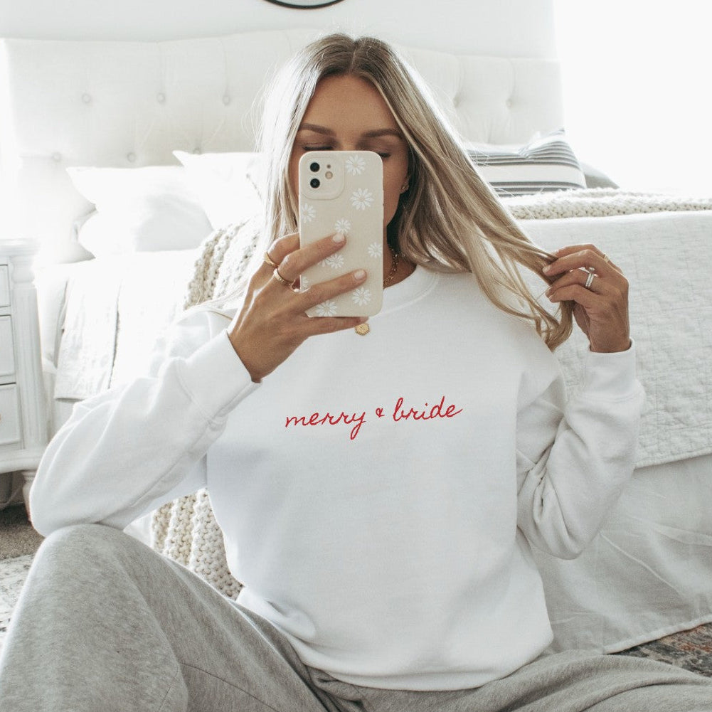 A soft white crewneck sweatshirt featuring elegant red script embroidery, ideal for a wedding-related celebration or cozy daily wear.