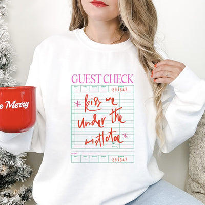 A white crewneck sweatshirt features a pink 'Guest Check' header and green lined receipt graphic with a festive handwritten phrase, perfect for holiday celebrations.