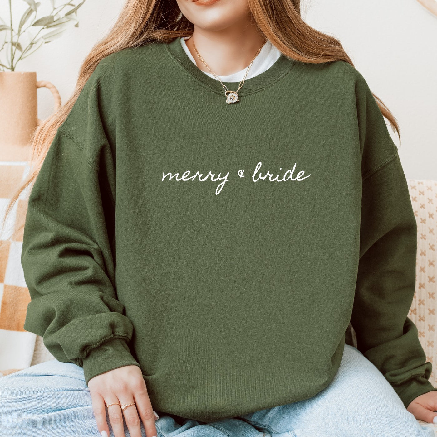 A dark green crewneck sweatshirt made of soft fabric features white script text, perfect for a festive bridal occasion.