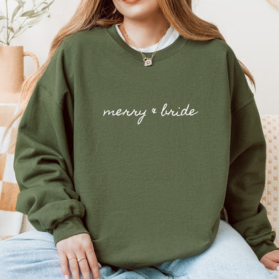 A dark green crewneck sweatshirt made of soft fabric features white script text, perfect for a festive bridal occasion.