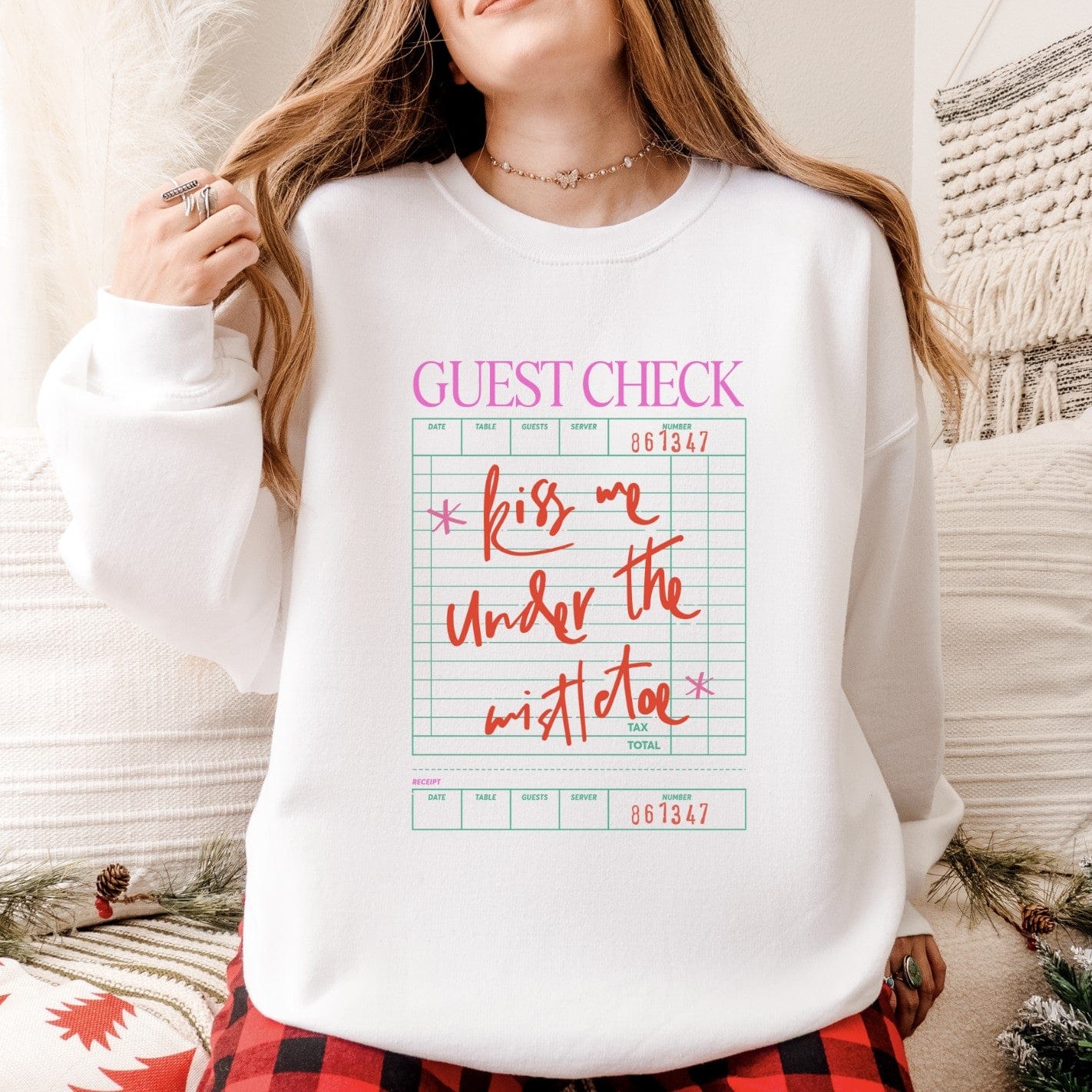 A white crewneck sweatshirt features a holiday-themed graphic resembling a guest check, making it a festive apparel item for the season.