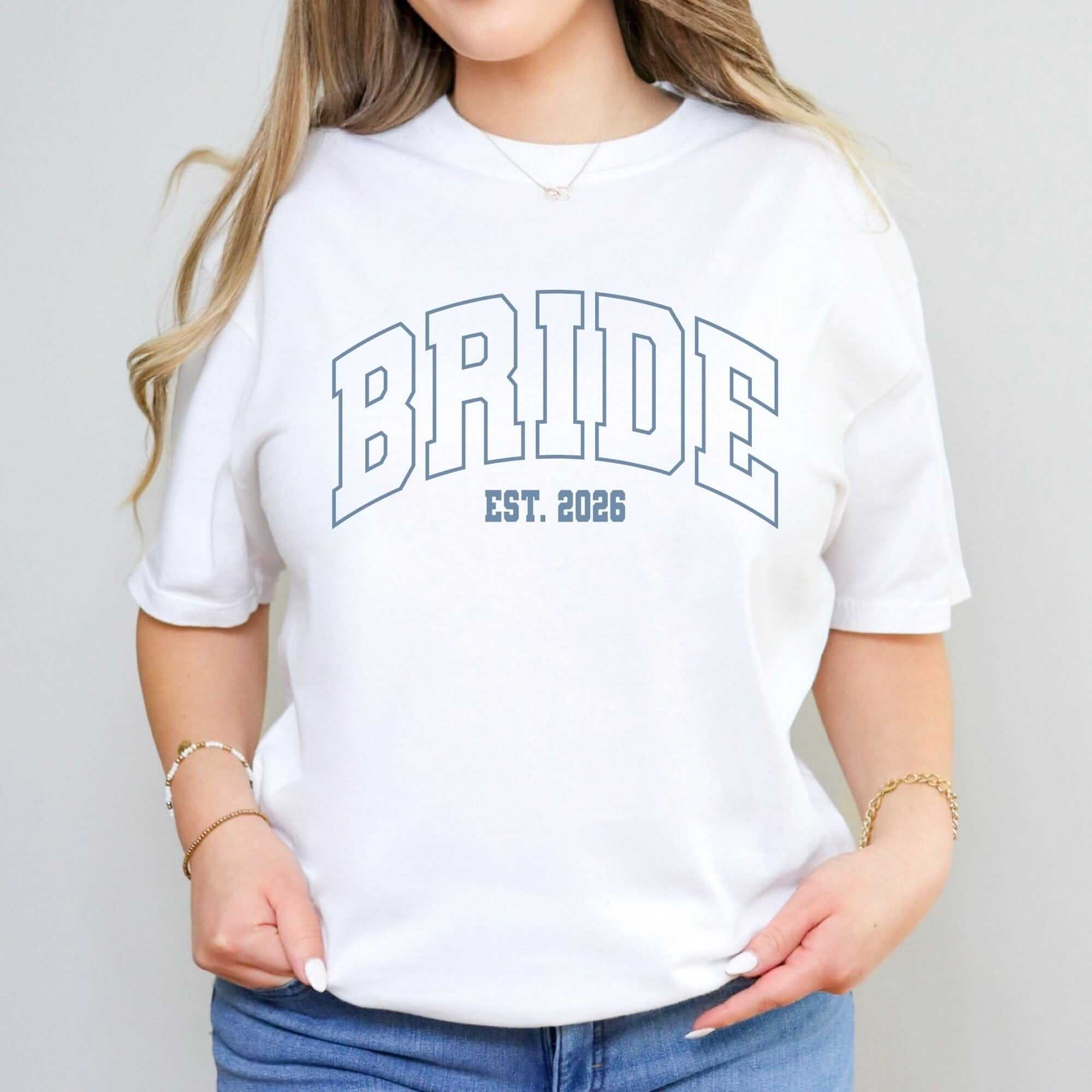 A white short-sleeve t-shirt made from a comfortable fabric, featuring collegiate style outlined text for a bride, perfect for pre-wedding events like a bridal shower or bachelorette party.