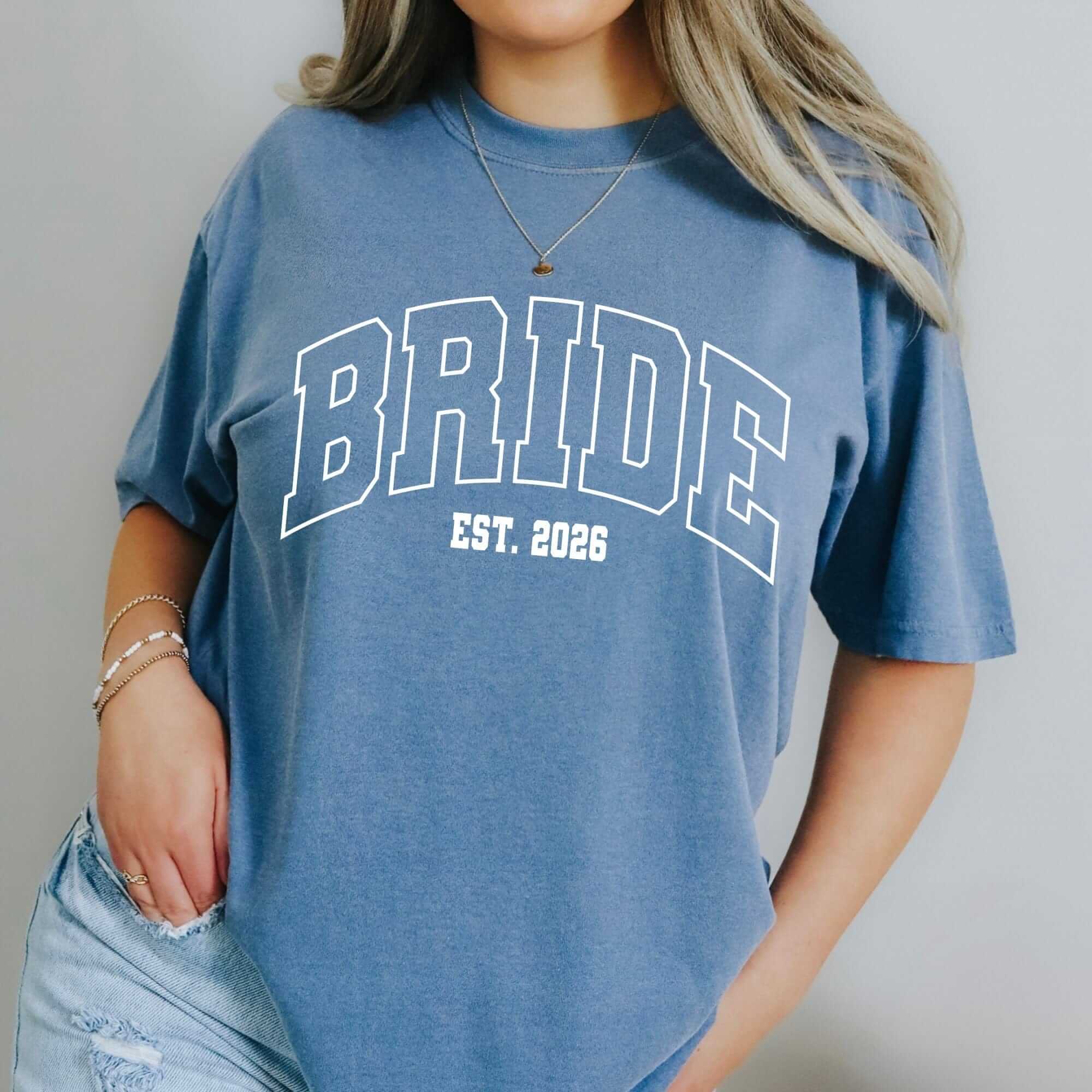 A comfortable, short-sleeve blue crewneck t-shirt features a large, arched white graphic design, ideal for a bridal celebration.
