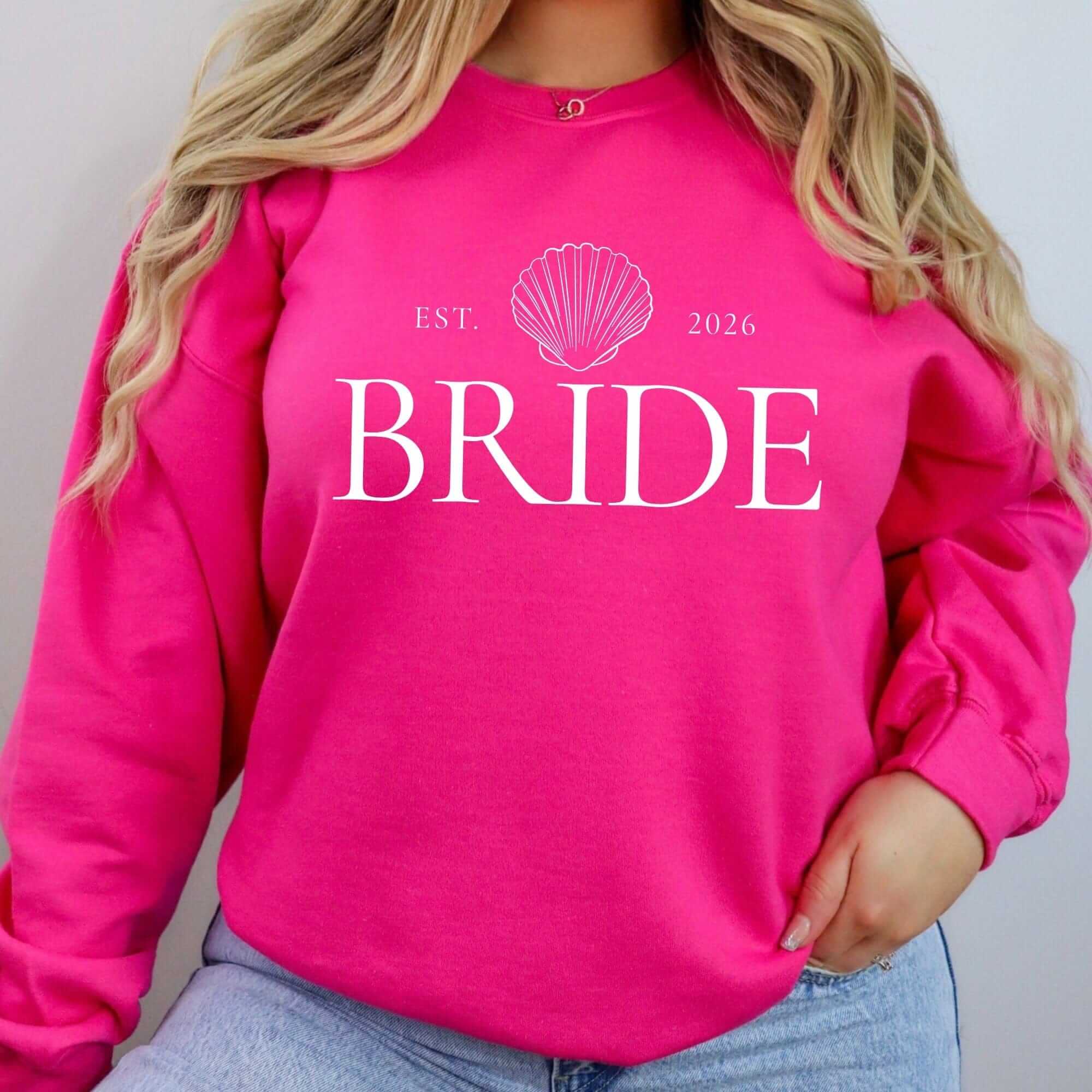 A bright pink crewneck sweatshirt made from soft fabric features a prominent white seashell graphic, ideal for bridal-themed occasions.