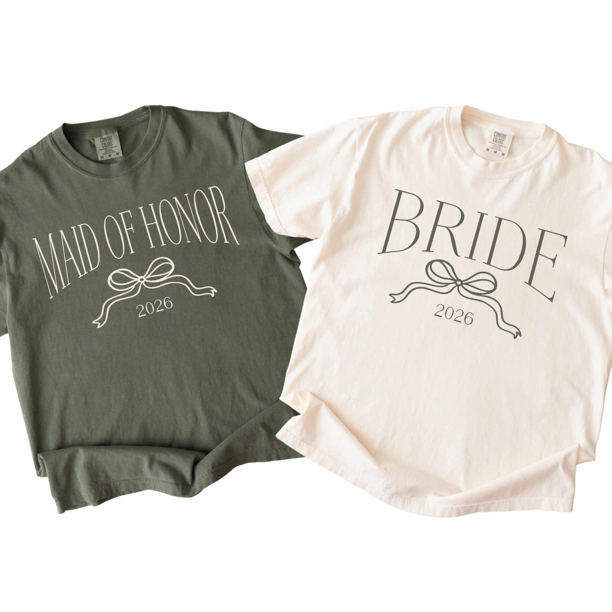 A set of two soft cotton short-sleeve t-shirts, one in muted olive green and one in cream, each featuring a coordinating graphic with an elegant ribbon and bow design, perfect for a wedding or bridal celebration.