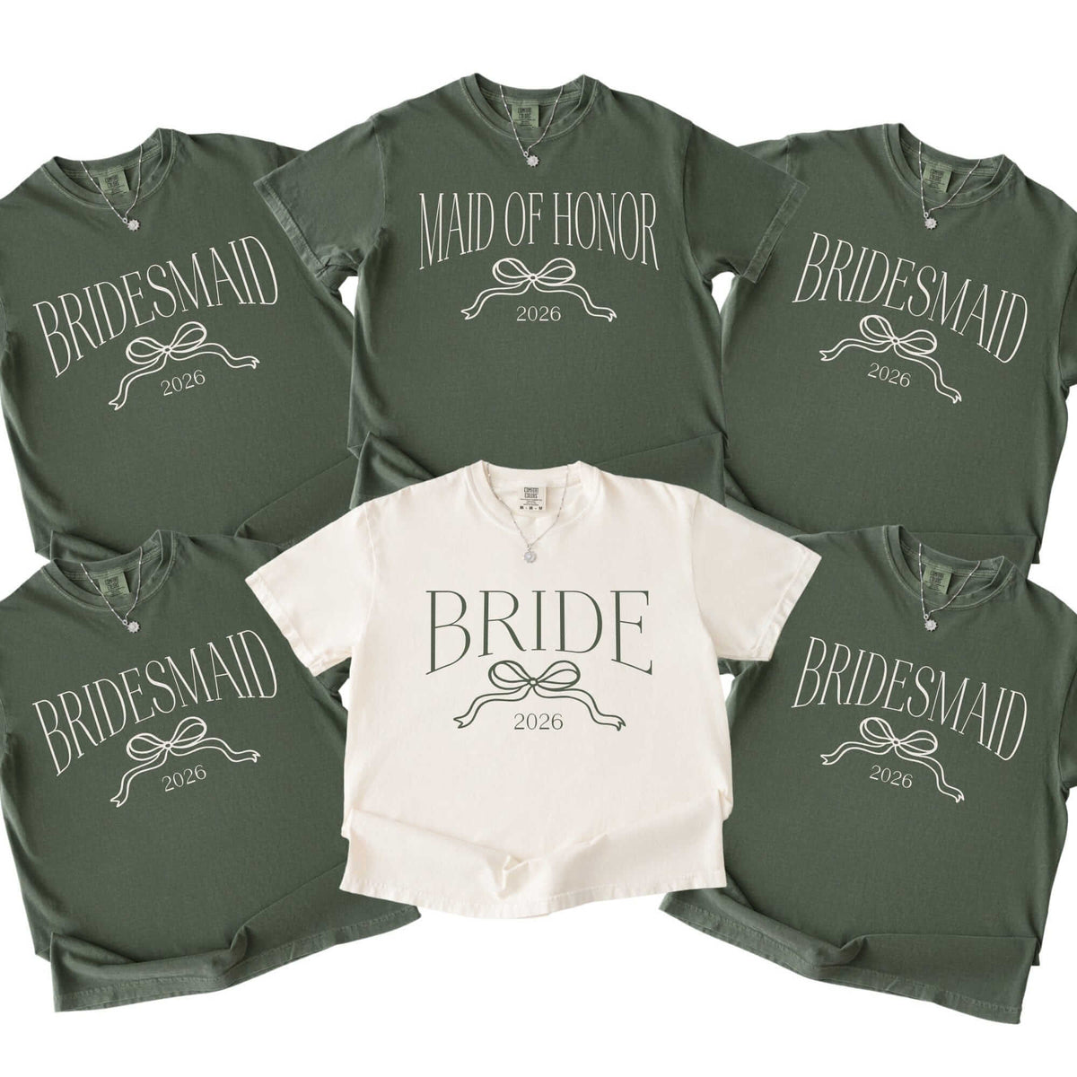 A collection of soft cotton-blend crewneck t-shirts, including one cream shirt and five dark green shirts, each adorned with a decorative bow graphic, ideal for a bridal party event.