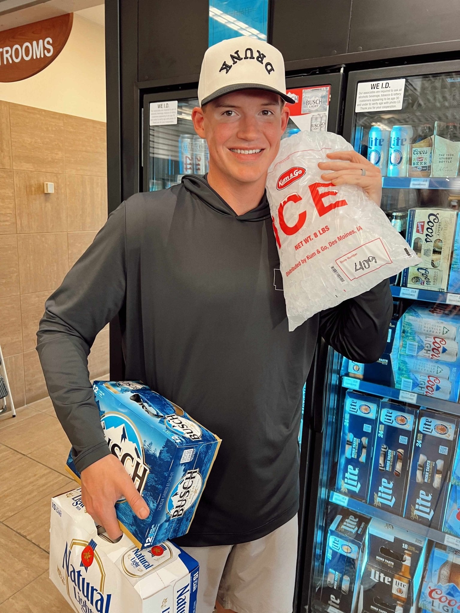 White trucker hat with red "DRUNK" text and colorful striped front panels, displayed by person holding beverages.