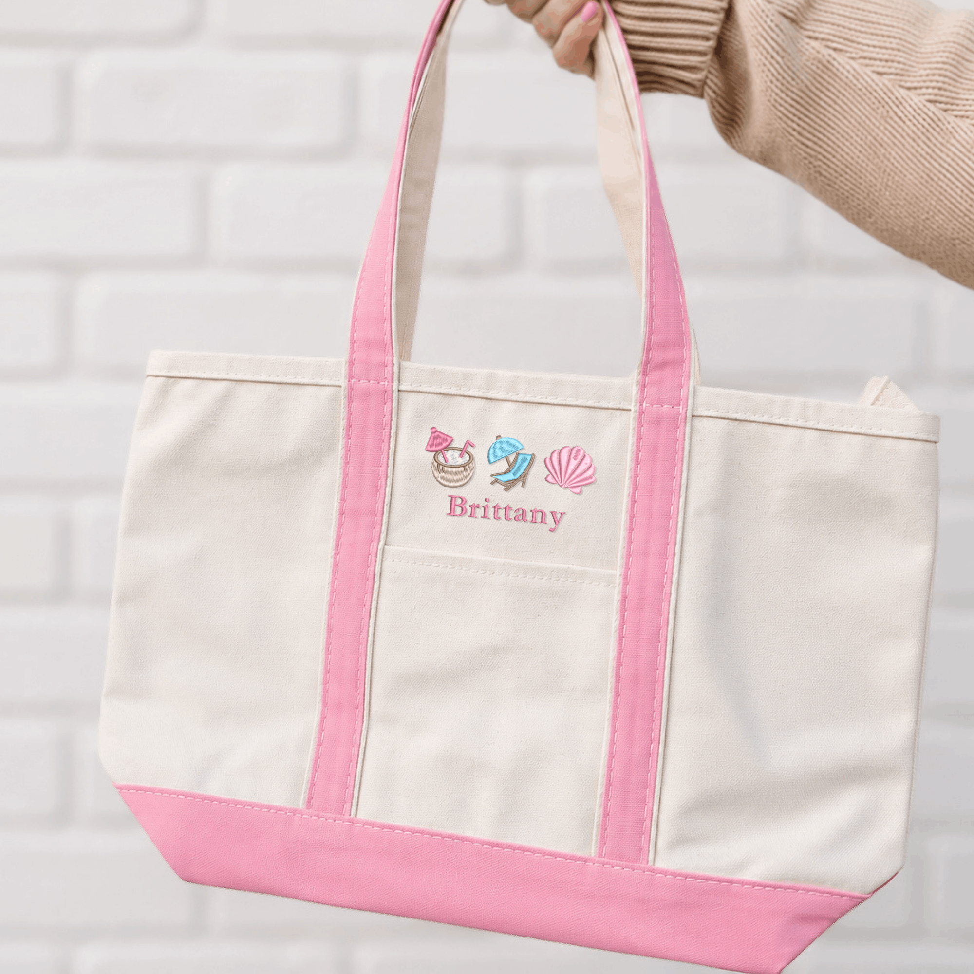 Personalized embroidered canvas tote bag with pink trim, the name Brittany, and coconut drink, beach chair, and seashell icons.