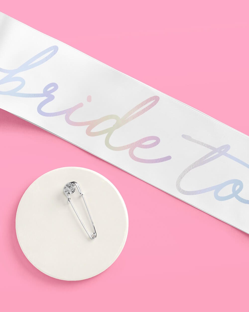 White sash with iridescent foil lettering and safety pin on pink background