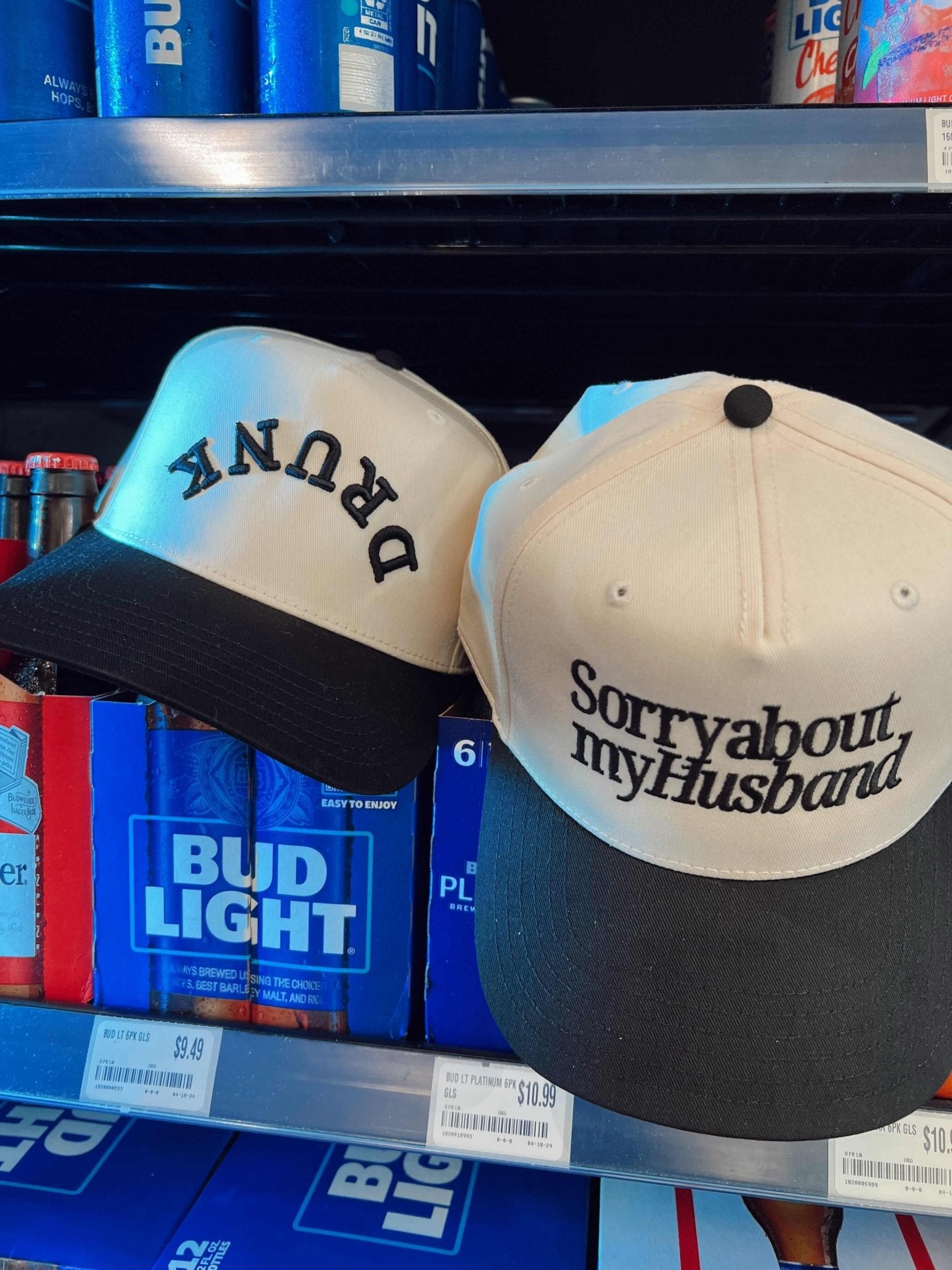 Vintage trucker hat with "DRUNK" text in blue and black colorway, displayed next to cream and black cap reading "Sorry about my Husband"