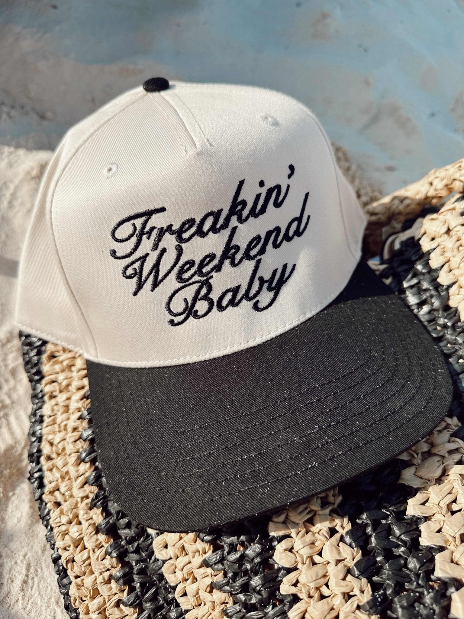 White and black vintage trucker hat with "Freakin' Weekend Baby" script text embroidered on front panel.