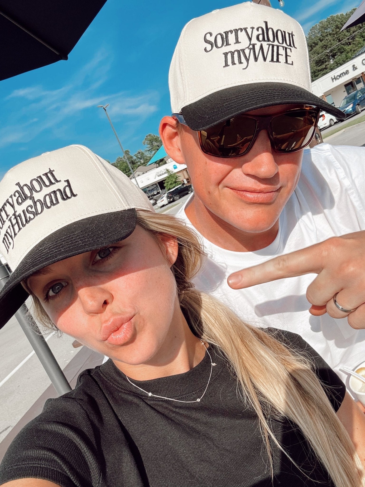 Couple wearing matching vintage trucker hats with black and white colorway; one hat reads "sorry about my husband" and the other reads "sorry about my wife"