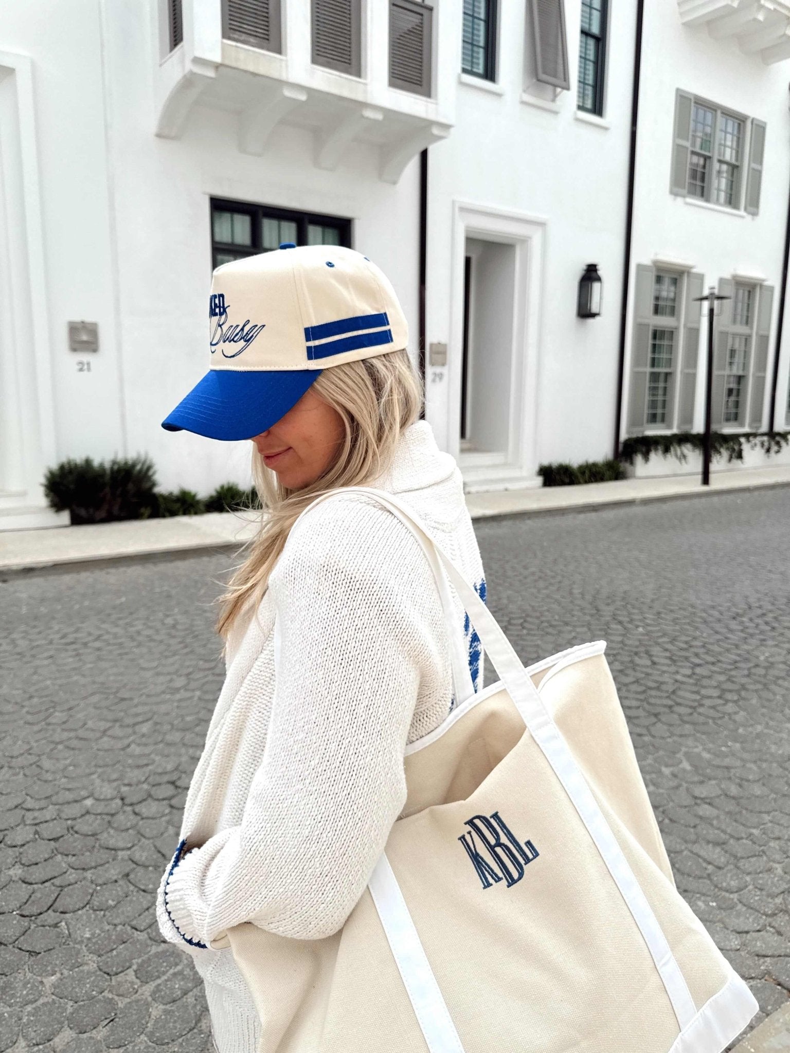 Woman wearing cream and royal blue vintage trucker hat with "Booked and Busy" text and striped design