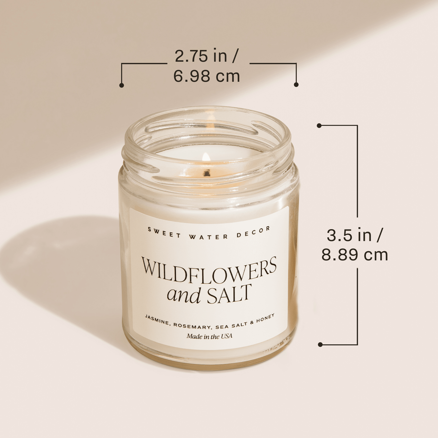 Clear glass jar candle with white label reading "Wildflowers and Salt" by Sweet Water Decor, cream colored soy candle with dimensions shown.