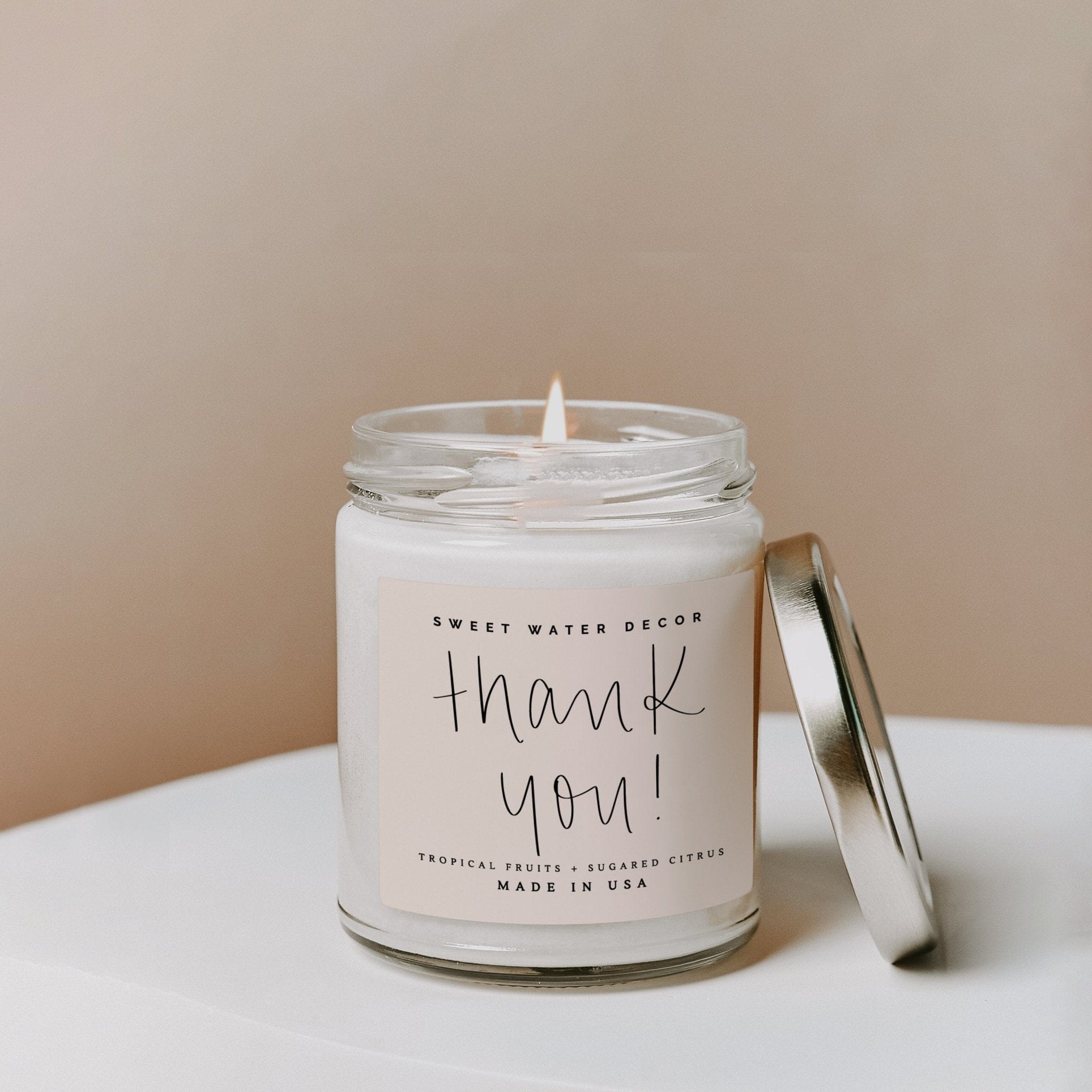 Clear glass jar candle with white soy wax and silver lid, featuring handwritten "thank you" text and "made in USA" label.