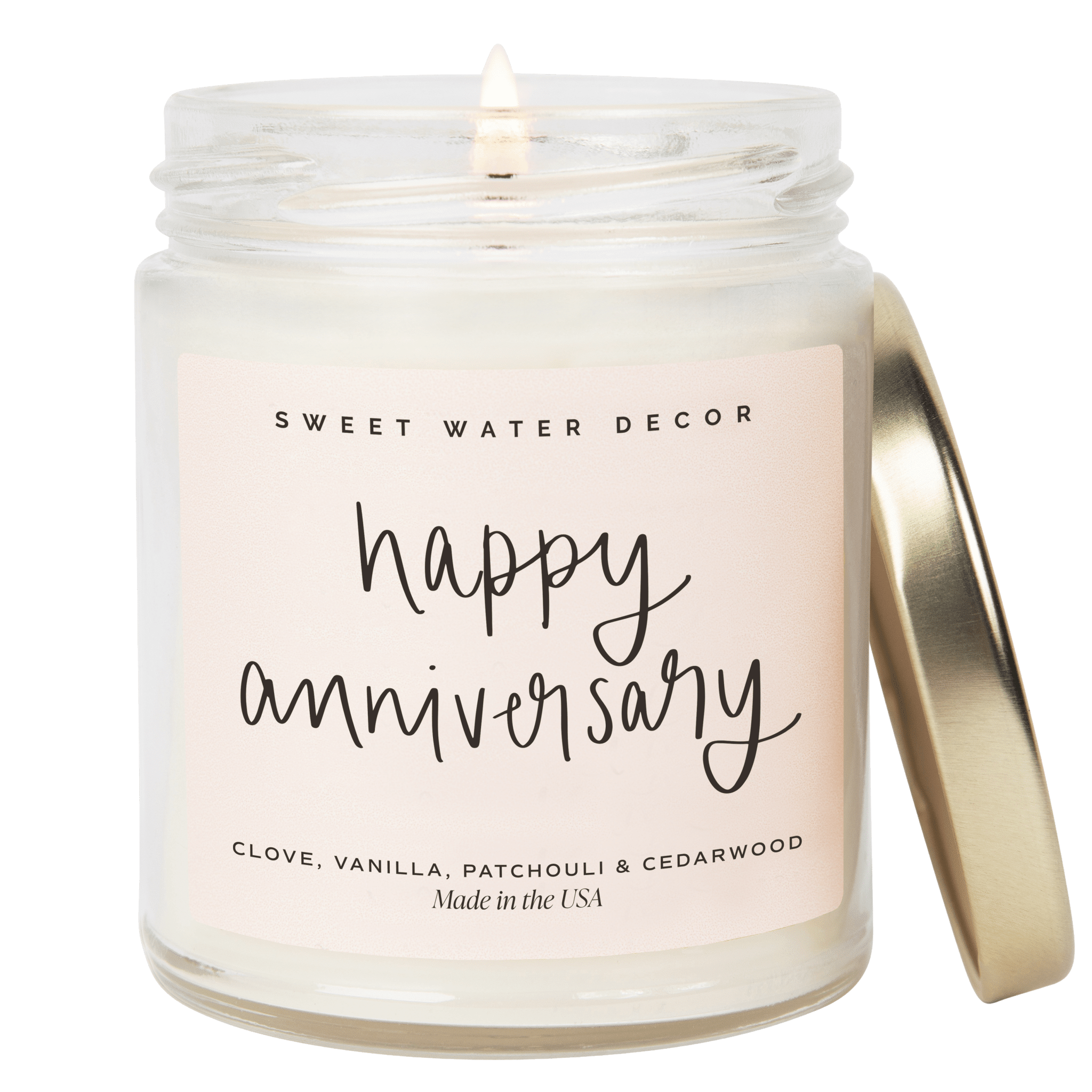 Clear glass jar candle with "happy anniversary" handwritten text, gold lid, and clove, vanilla, patchouli & cedarwood scent label by Sweet Water Decor.