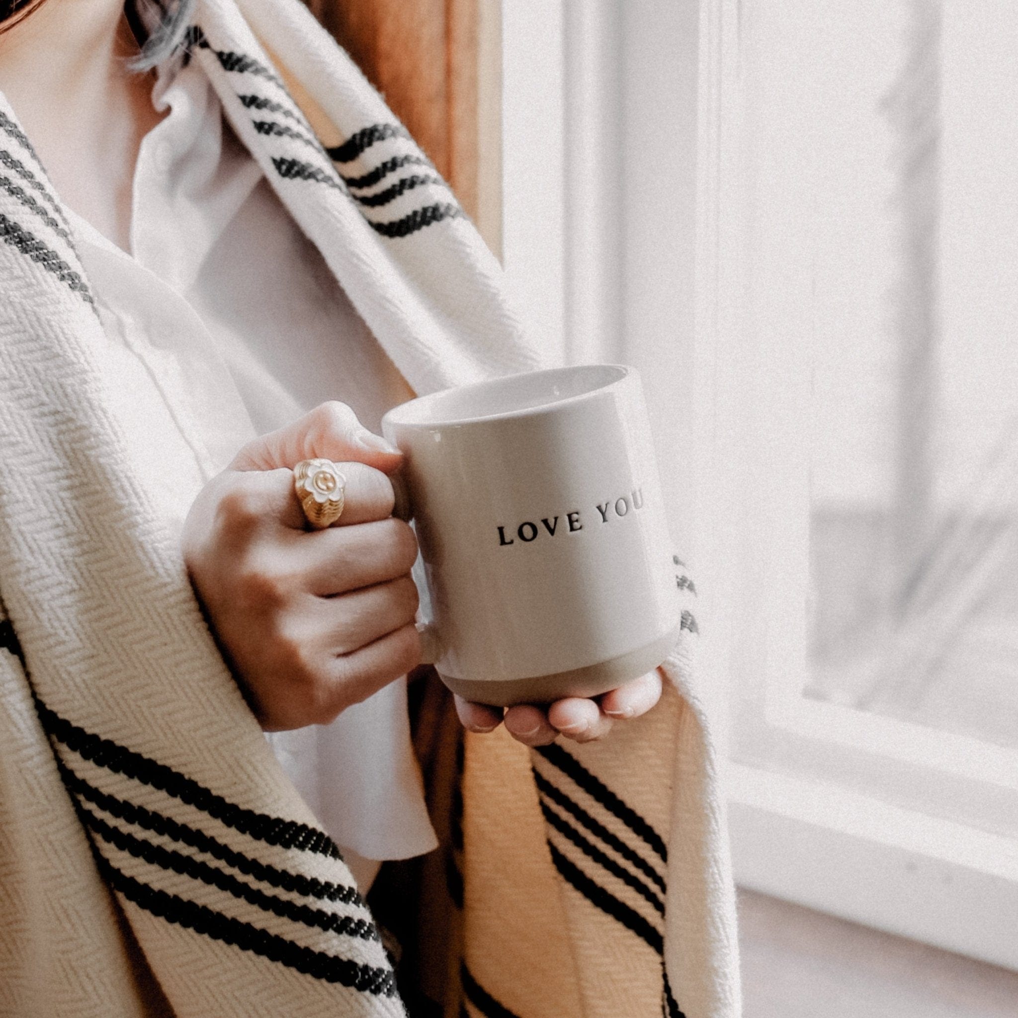 White ceramic mug with "LOVE YOU" text, held in hands wearing striped cardigan